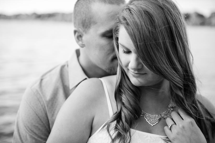 a black and white engagement photo of a man kissing a woman's cheek with the thames river behind them at fanshawe conservation area