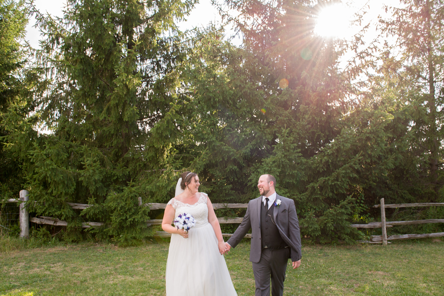a bride and groom laugh while walking hand in hand through a field