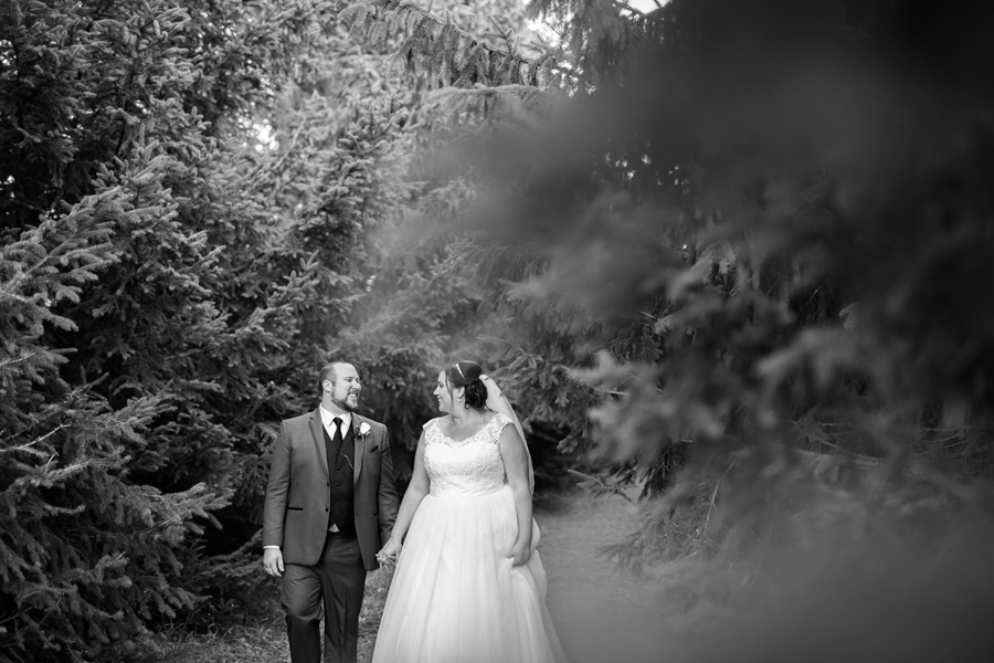a bride and groom walk through trees holding hands