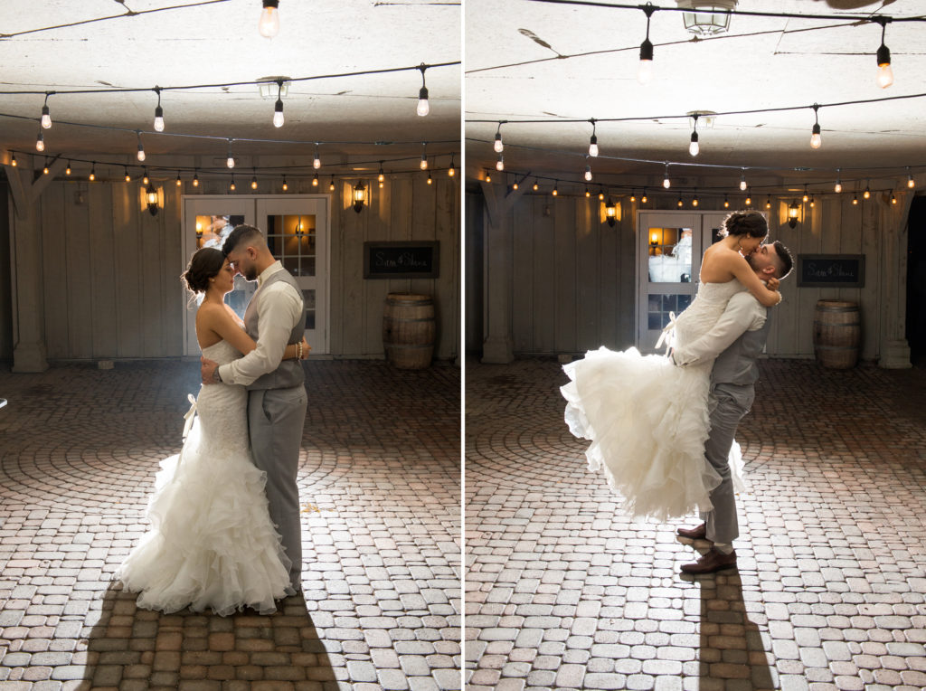 a groom lifts his bride up for a kiss under outdoor lights at night