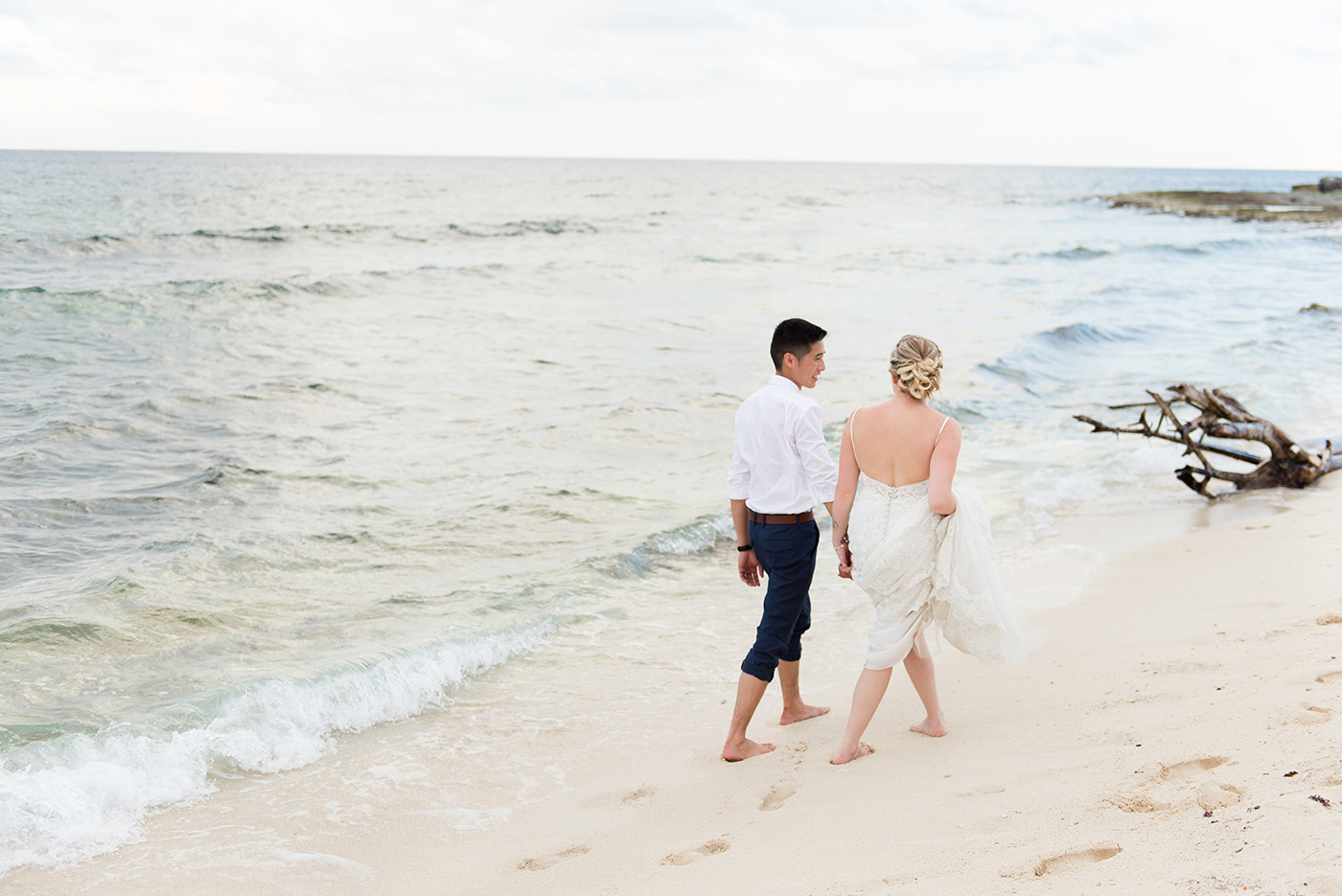 a bride and groom walk down the beach in cancun, mexico after their destination wedding in riviera maya