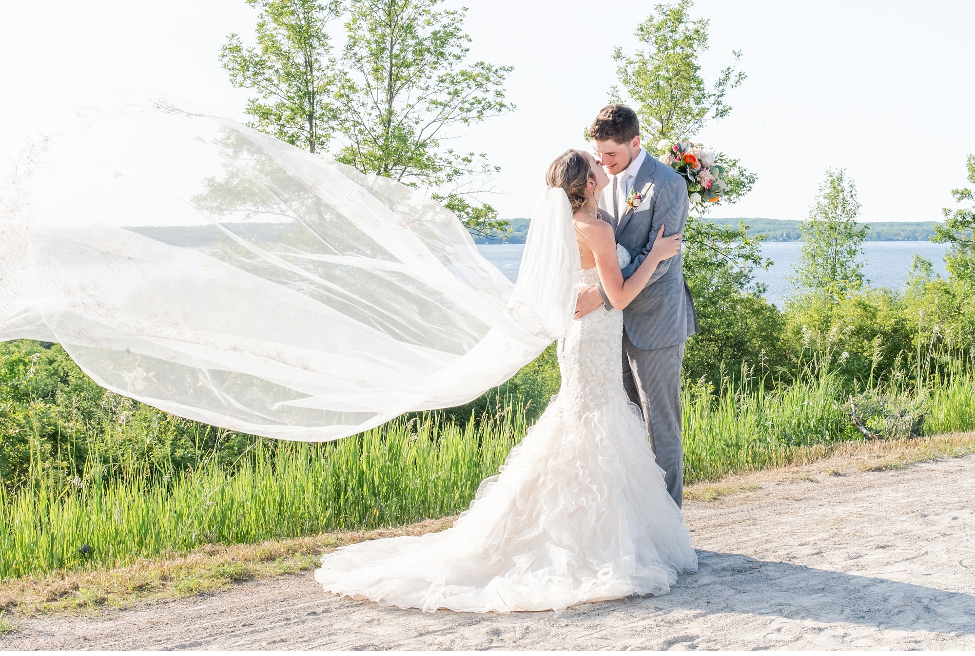 bride's veil blows in the wind as she and the groom kiss at a kawartha lakes wedding