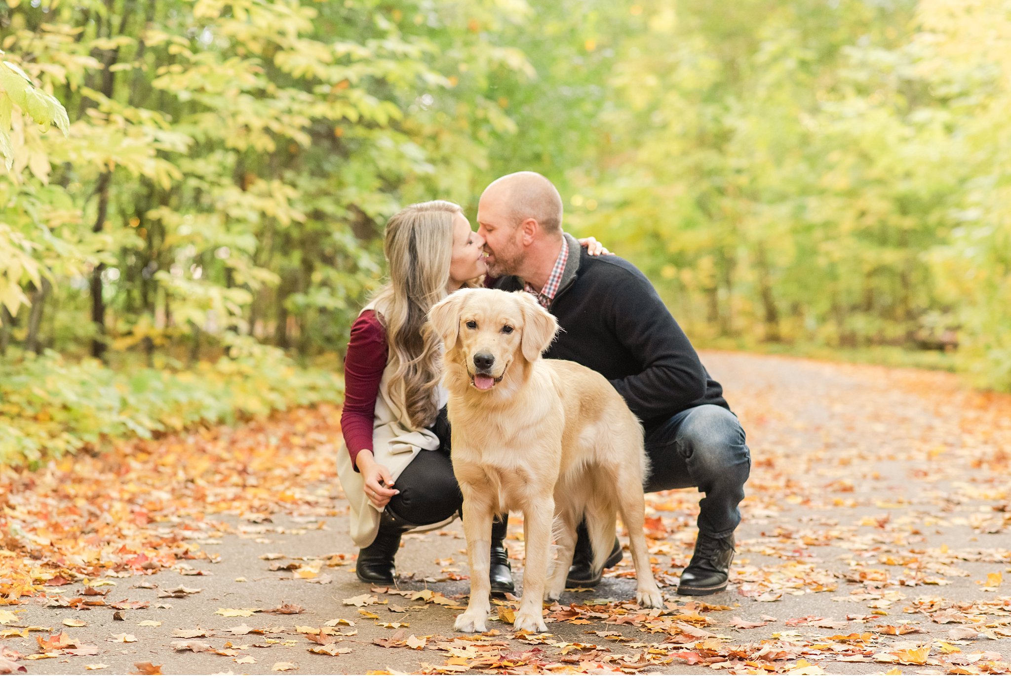 a couple kisses kneeling with their dog