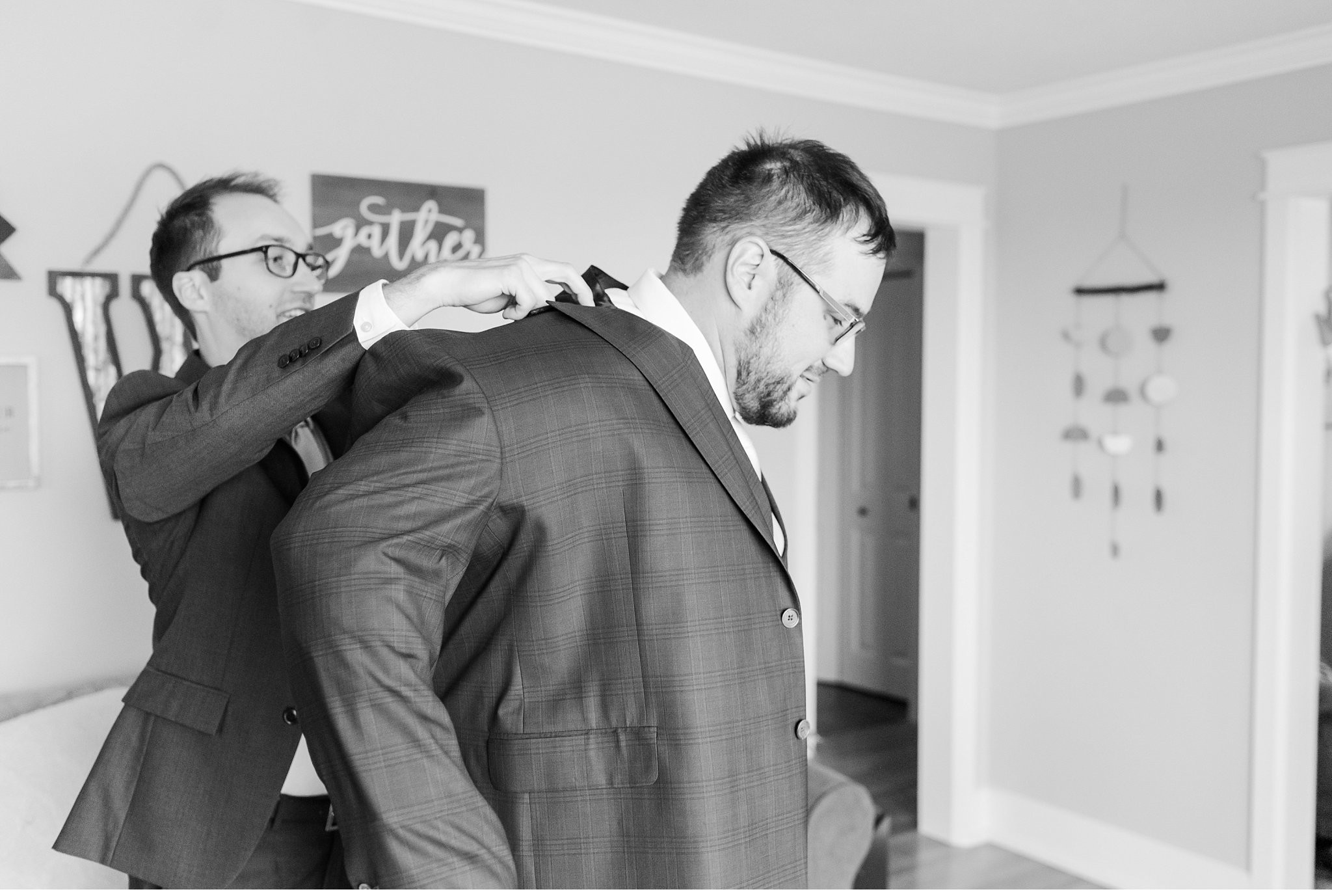 groomsman helps groom get his jacket on