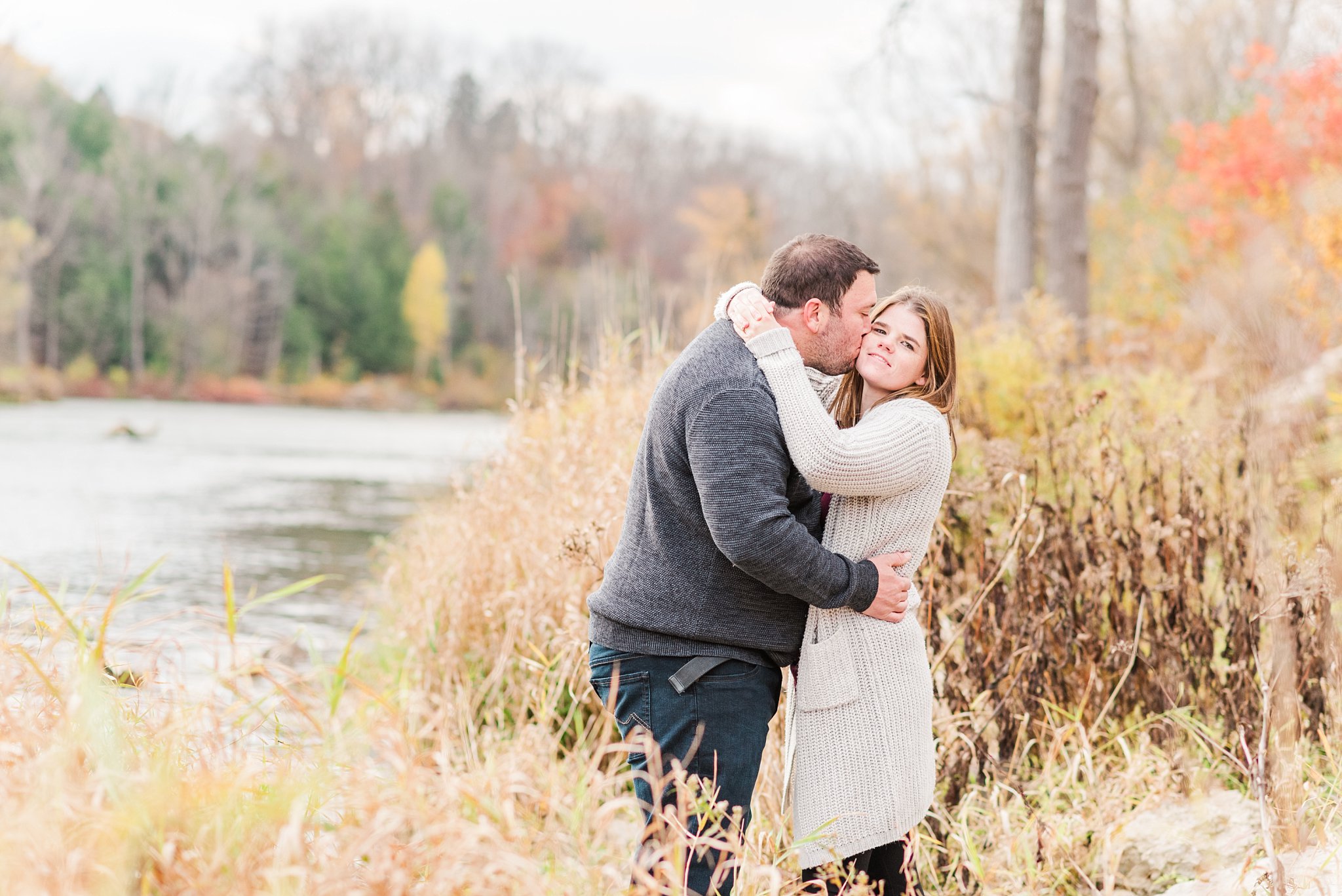 a couple kisses on the edge of the thames river at fanshawe conservation area during their engagement session, london ontario wedding photographer