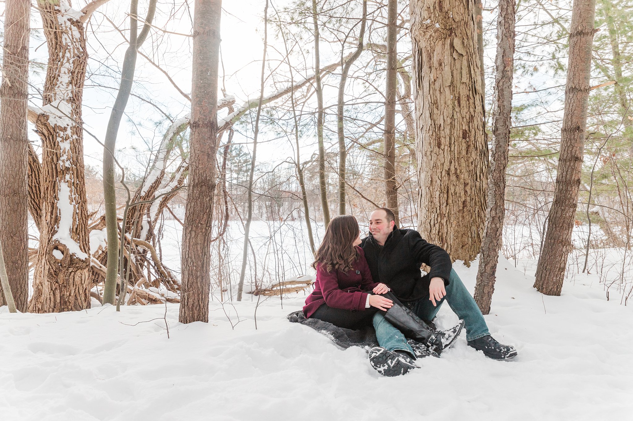 a couple sits on a blanket in the snow during their engagement session by london ontario wedding photographers life is beautiful photography