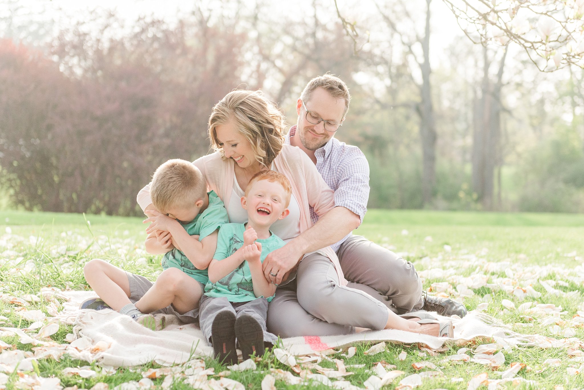 parents lean in and tickle their sons as they all sit on a blanket in springbank park by london ontario family photographer life is beautiful photography