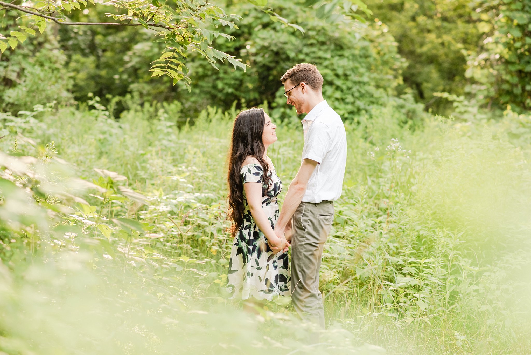 a couple holds hands facing one another and laughing together in a meadow at rock glen conservation area during their engagement session by london ontario wedding photographer life is beautiful photography