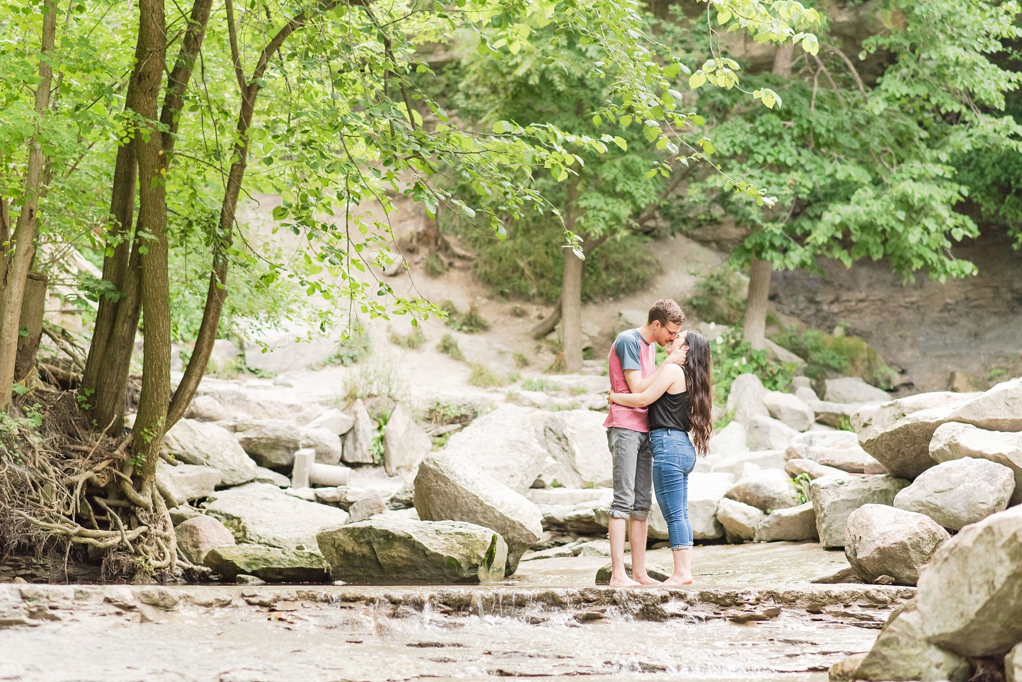 a couple kisses while standing in front of a waterfall at rock glen conservation area a couple kisses at rock glen conservation area during their engagement session by london ontario wedding photographer life is beautiful photography