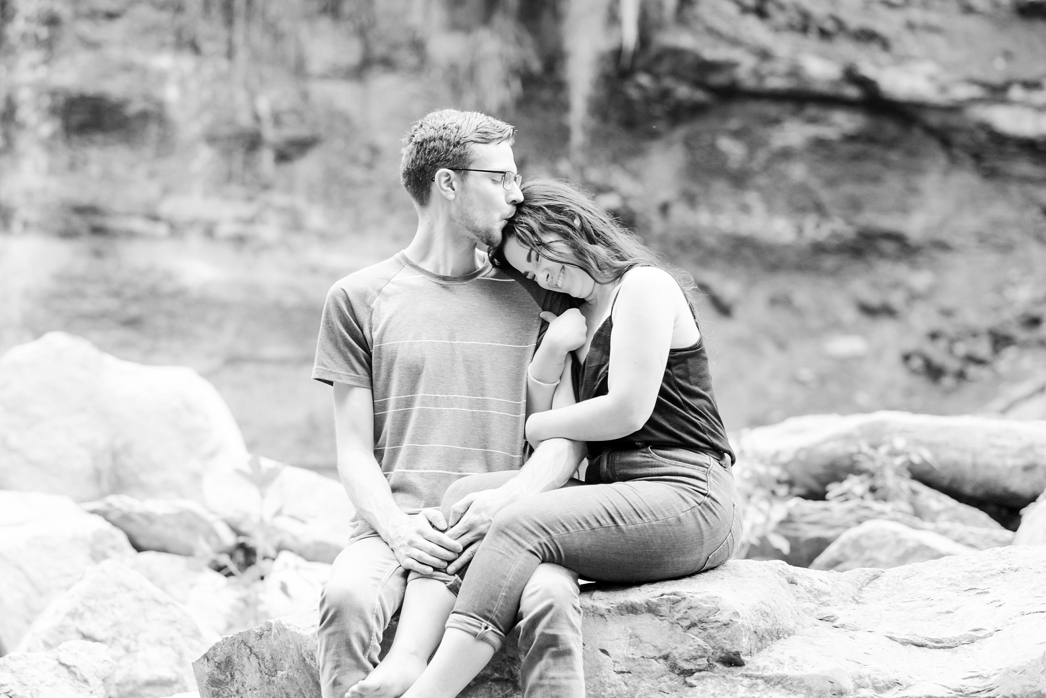 a man kisses a woman's head while sitting on a rock at rock glen conservation area