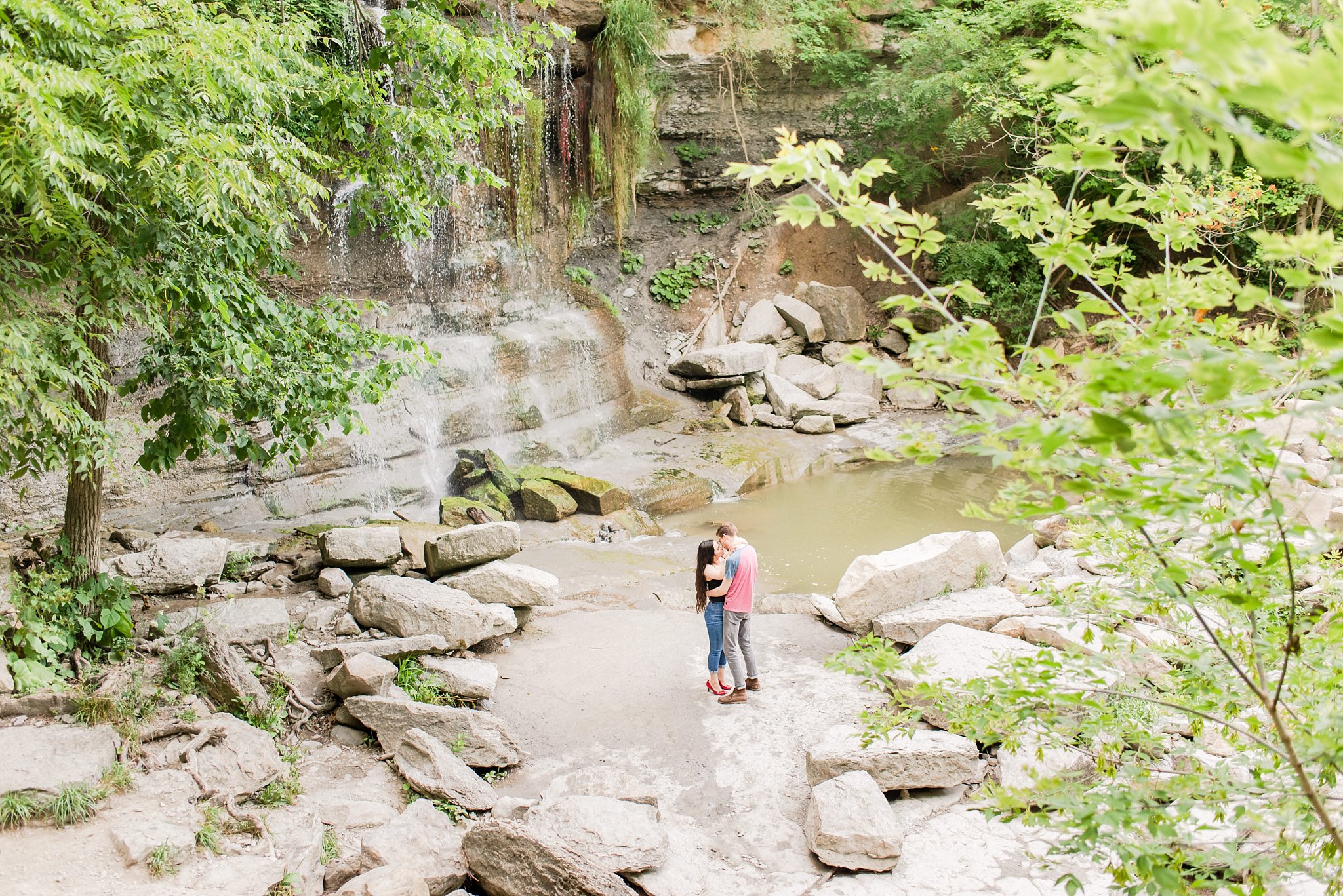 a couple kisses while standing at the base of a waterfall at rock glen conservation area a couple kisses while standing in front of a waterfall at rock glen conservation area a couple kisses at rock glen conservation area during their engagement session by london ontario wedding photographer life is beautiful photography