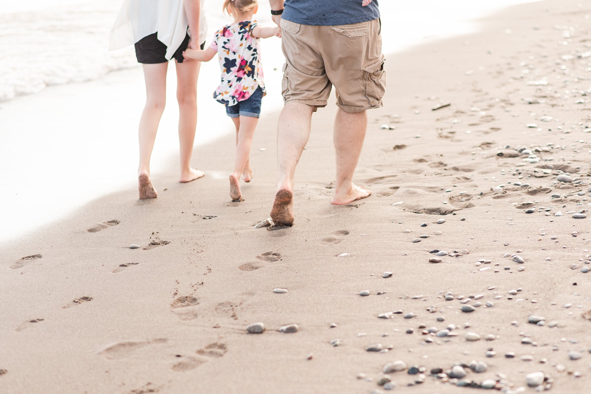 a close-up of a family's feet as they hold hands and walk down the beach together in Port Stanley