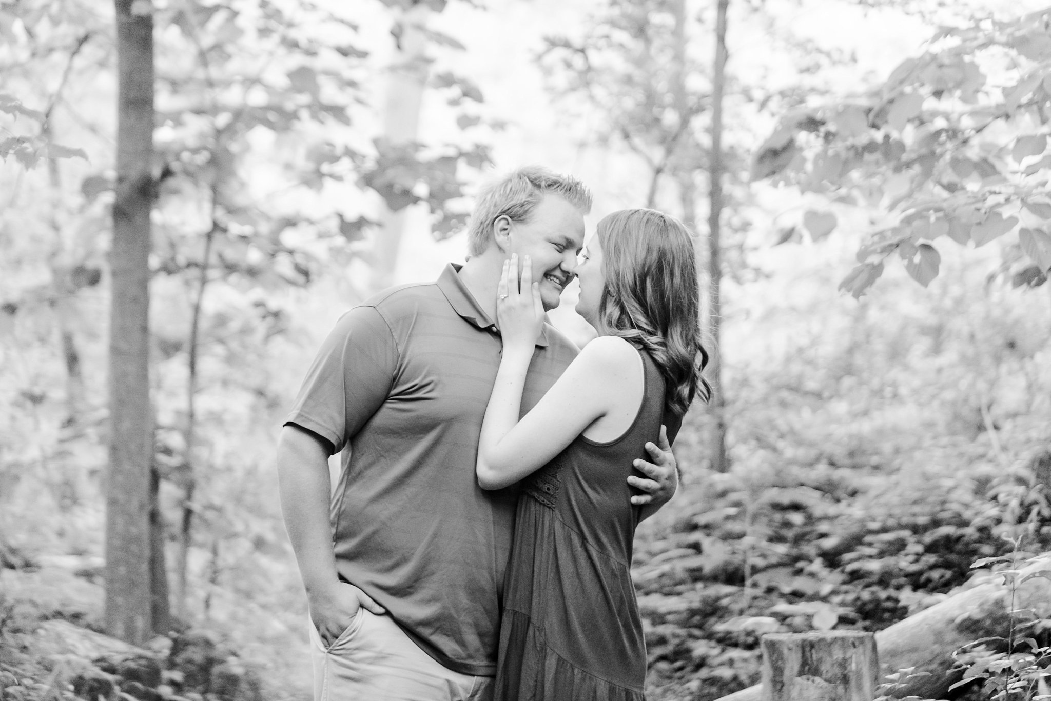 a black and white photo of a couple surrounded by trees. the man is wrapping his arms around the woman's wait, and she is reaching up to his jaw as they lean in for a kiss. wedding photographers in london ontario life is beautiful photography