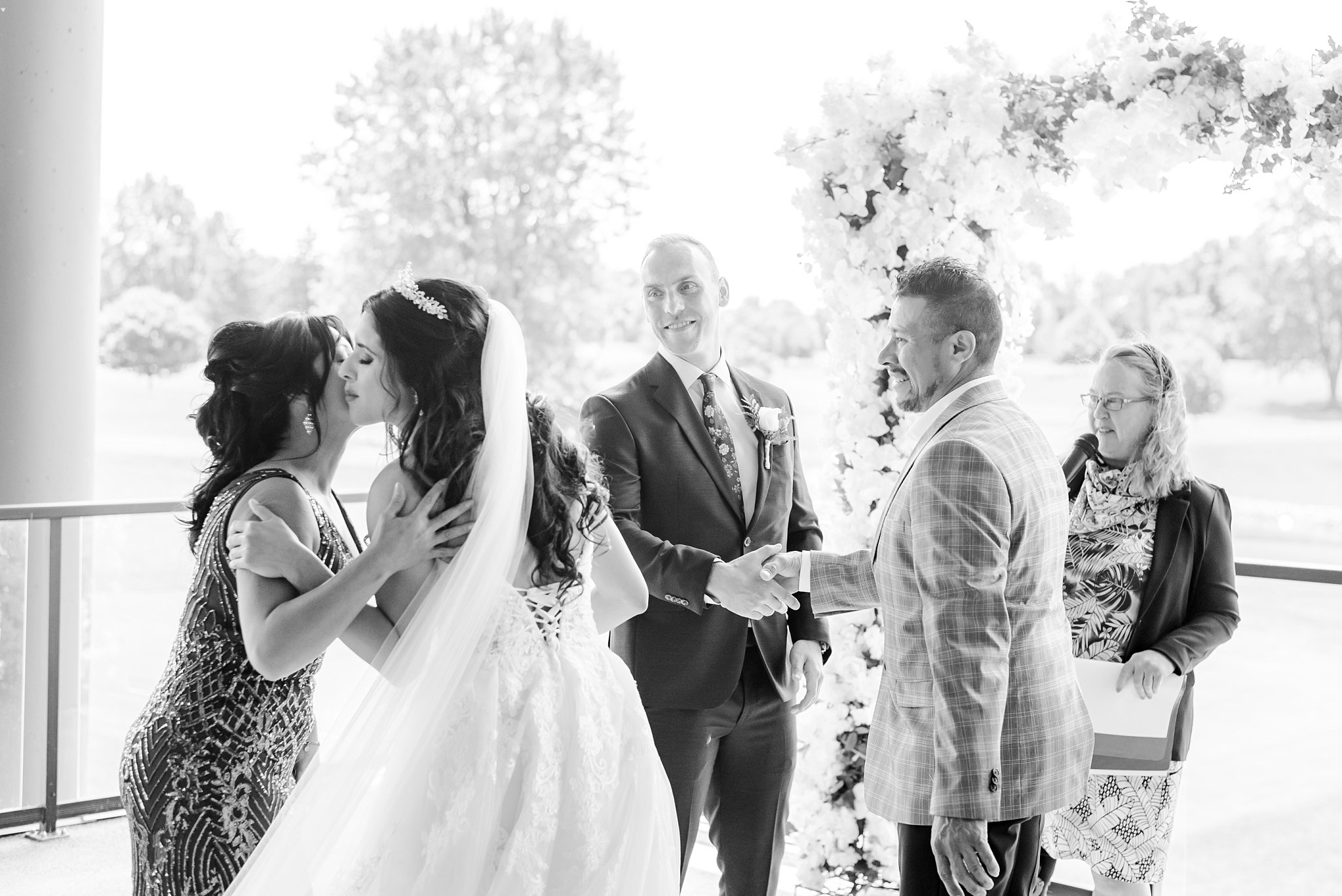 a bride kisses her mom, the groom shakes her dad's hand at their wedding ceremony