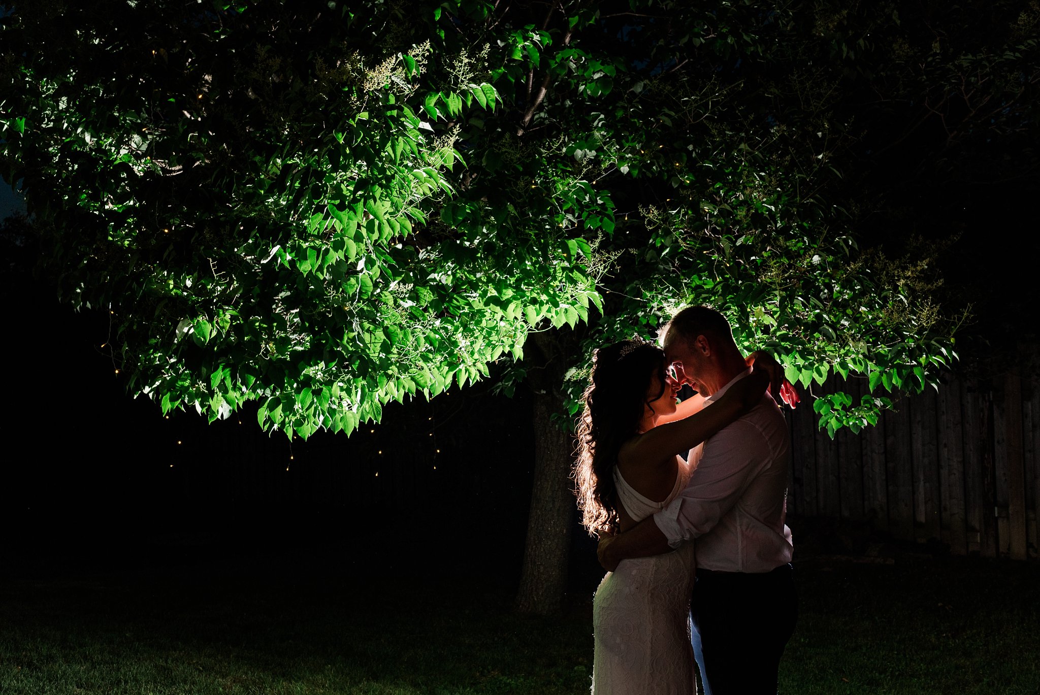 a night photo of the bride and groom hugging, with a light behind illuminating them and a tree  kelowna wedding photographer