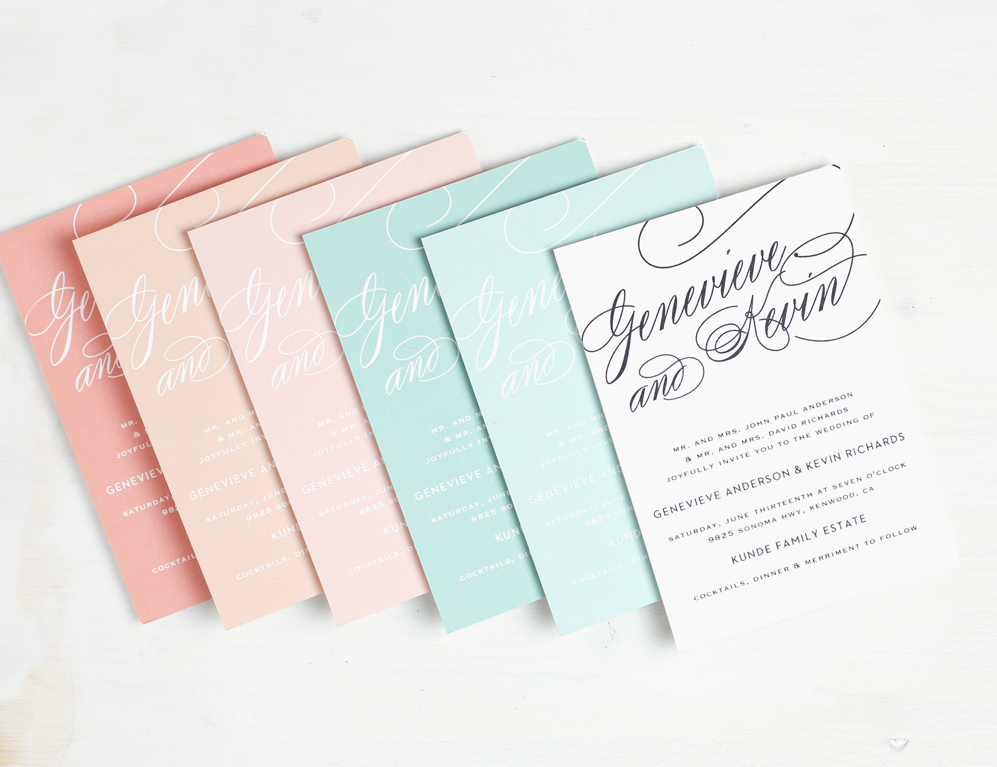 pink, blue, green and white wedding invitations lay atop one another