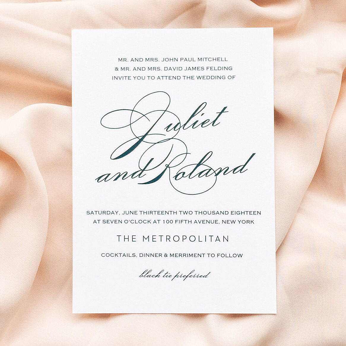 white wedding invitation with black calligraphy lays on a soft pink cloth