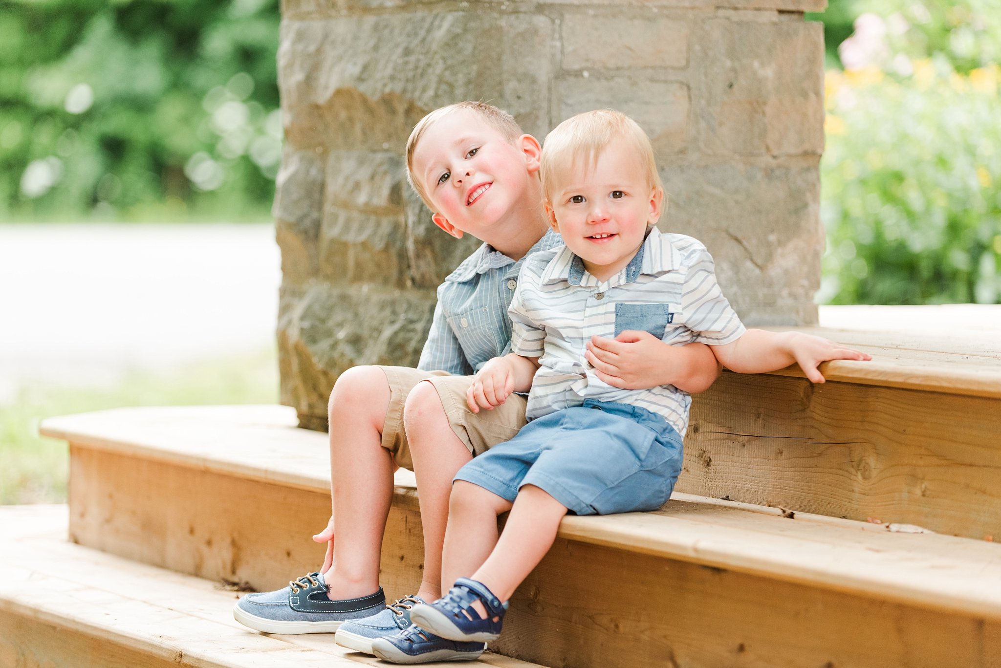 two little boys with blonde hair sit on wooden steps