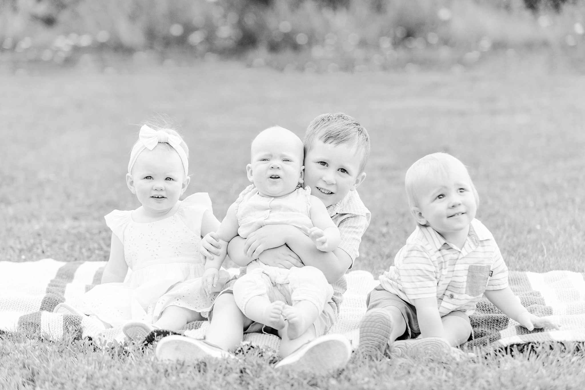 a black and white photo of four children sitting on a blanket