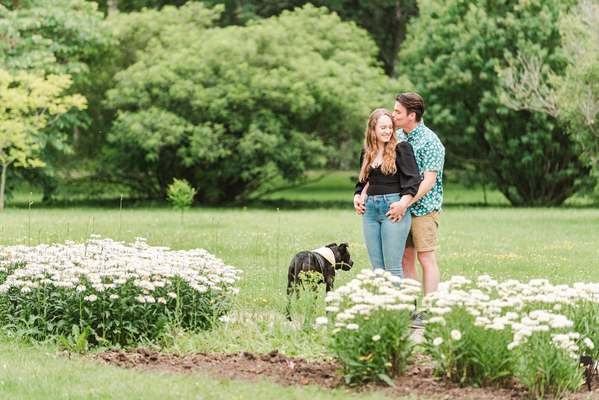 a couple stands in a garden with their dog at guelph arboretum