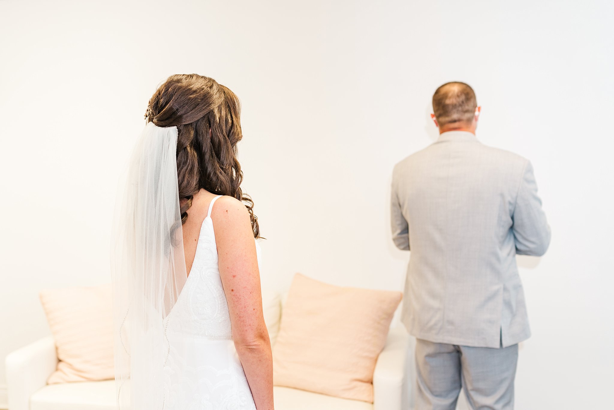 a bride stands behind a groom, who has his back turned for their first look