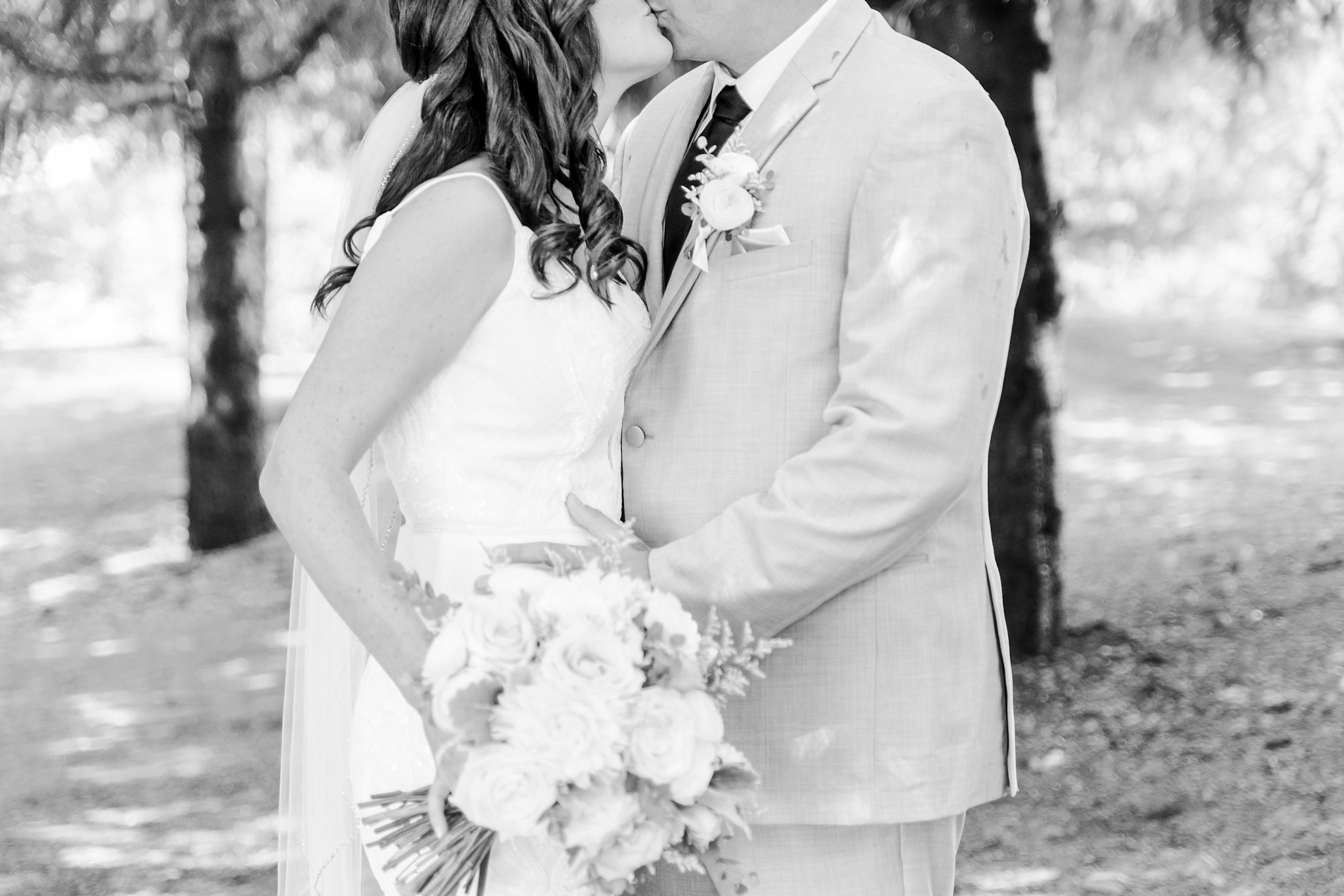 a black and white photo of a bride and groom kissing. their heads are cut off at the top. the bride is holding a bouquet.