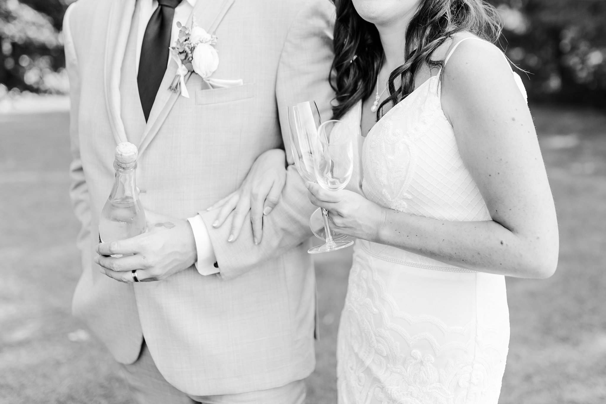 a black and white close up photo of a bride and groom. the groom is holding a bottle of champagne and the bride is holding two champagne flutes
