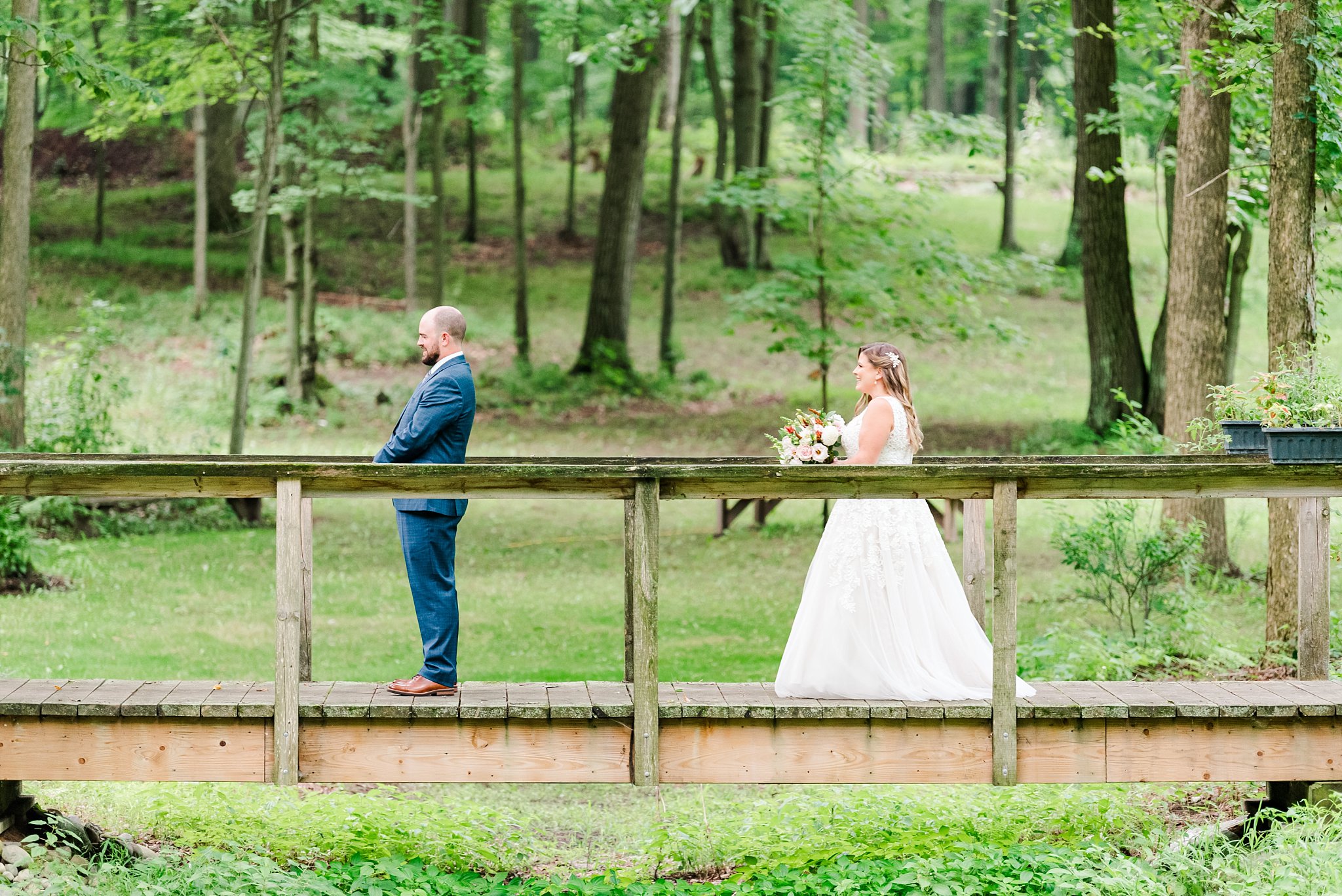 a bride walks up behind a groom on a wooden bridge at fernwood hills for their first look