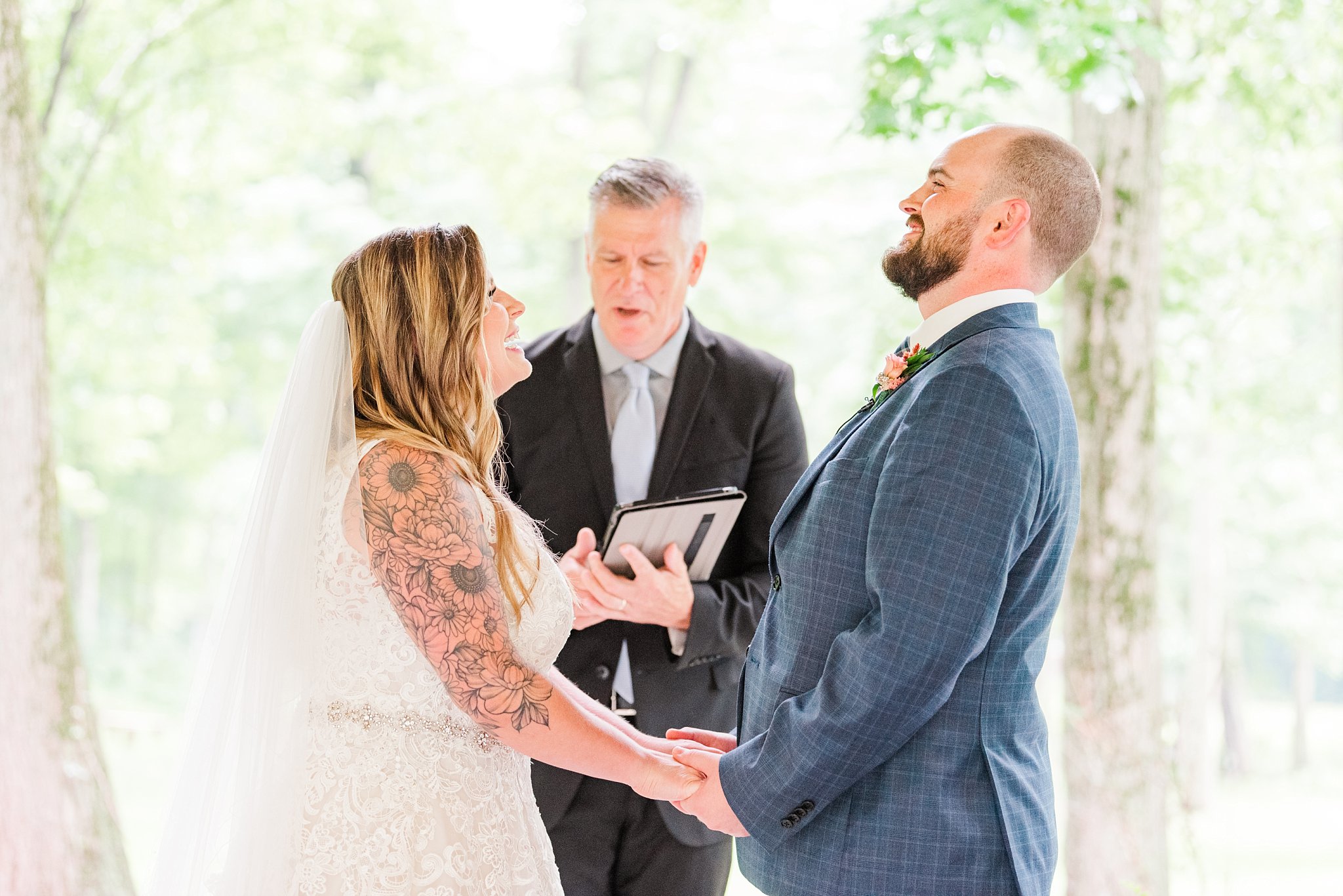 a bride and groom hold hands and smile while their officiant speaks behind them