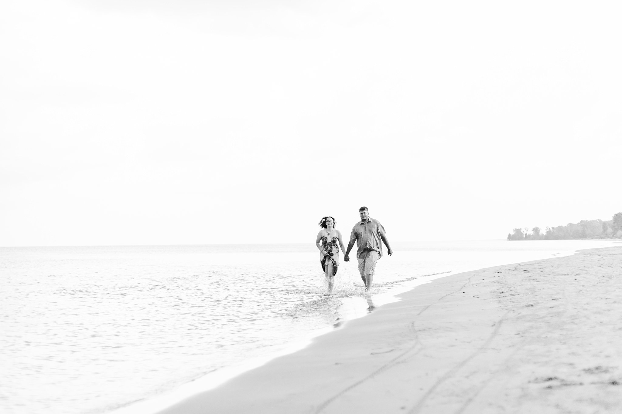 a couple holds hands and runs through the water together at ipperwash beach
