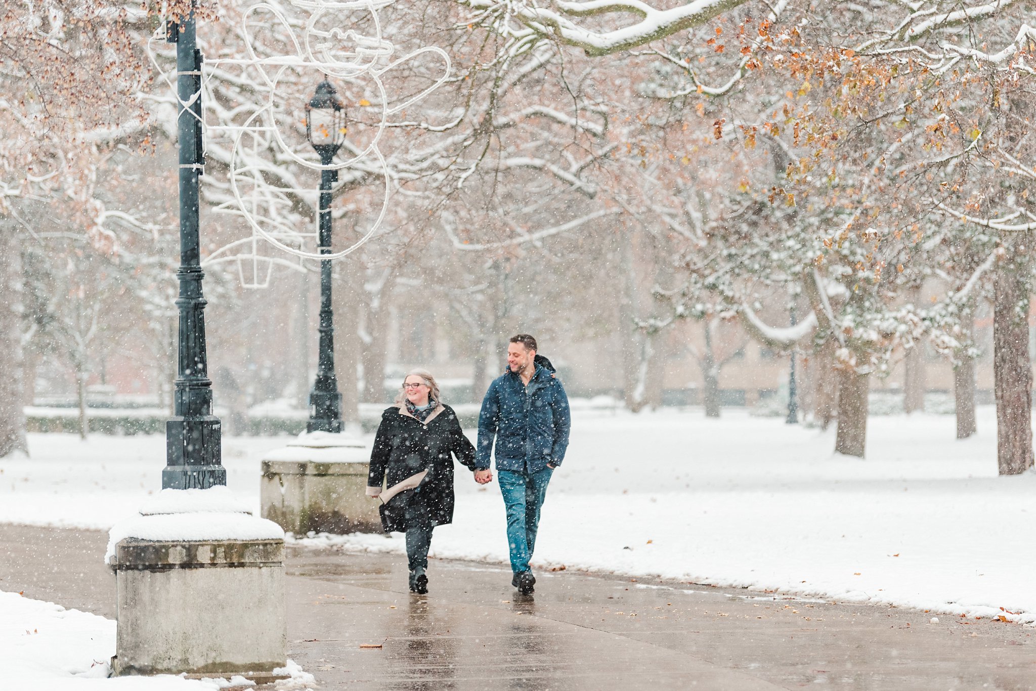 a couple walks along the path in victoria park while it's snowing heavily