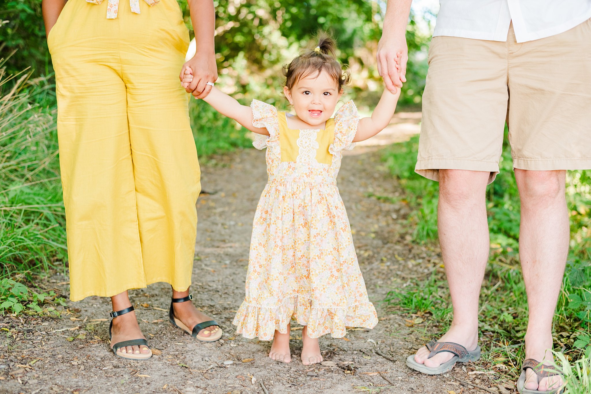 a little girl smiles while holding hands with her mom and dad
