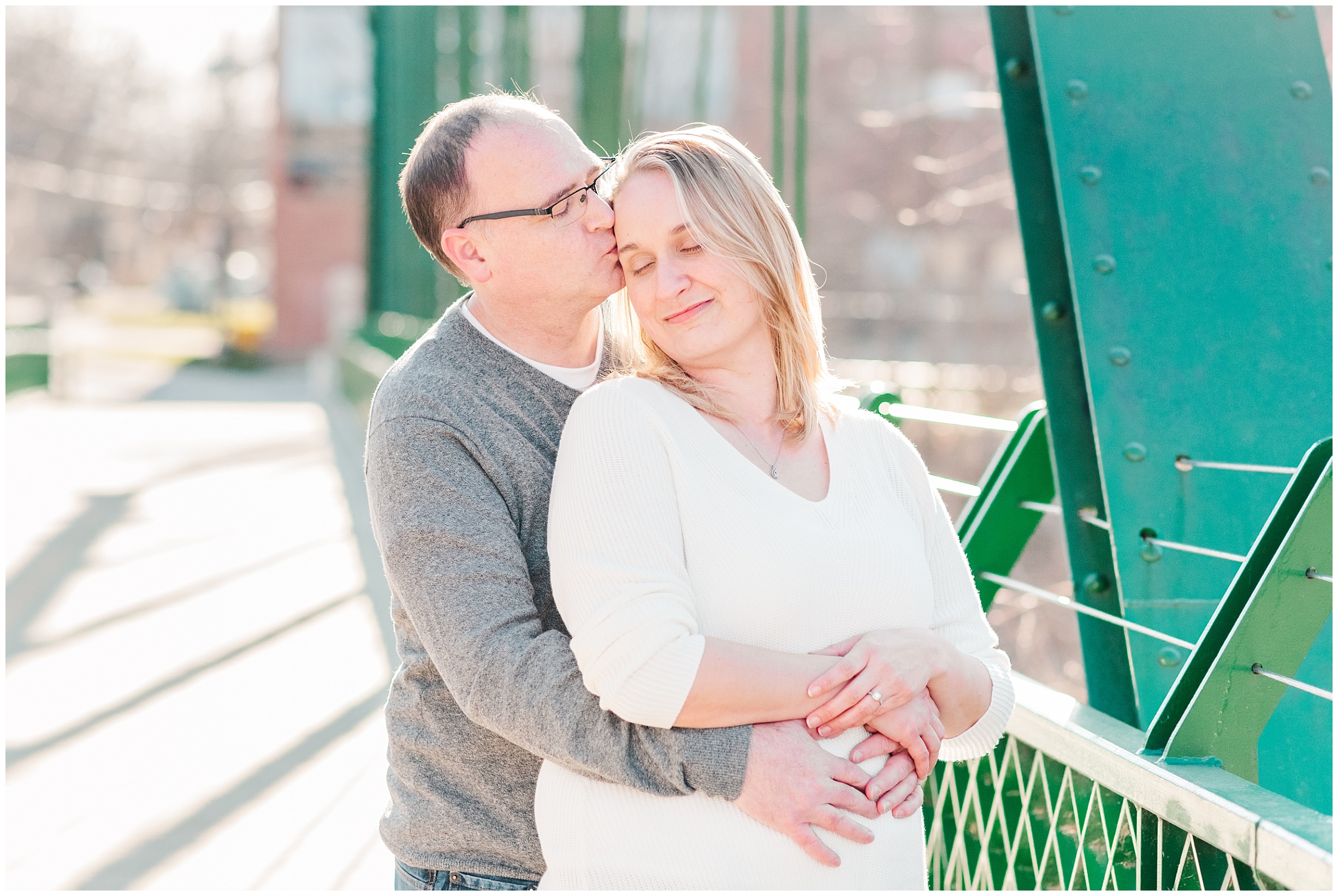 a man wraps his arms around a woman and kisses her forehead while standing on a bridge by st thomas ontario photographers life is beautiful photography