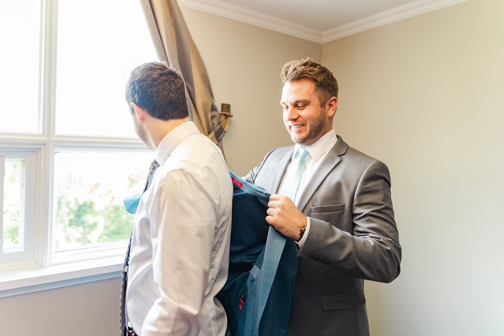 a groomsman helps a groom get his suit jacket on