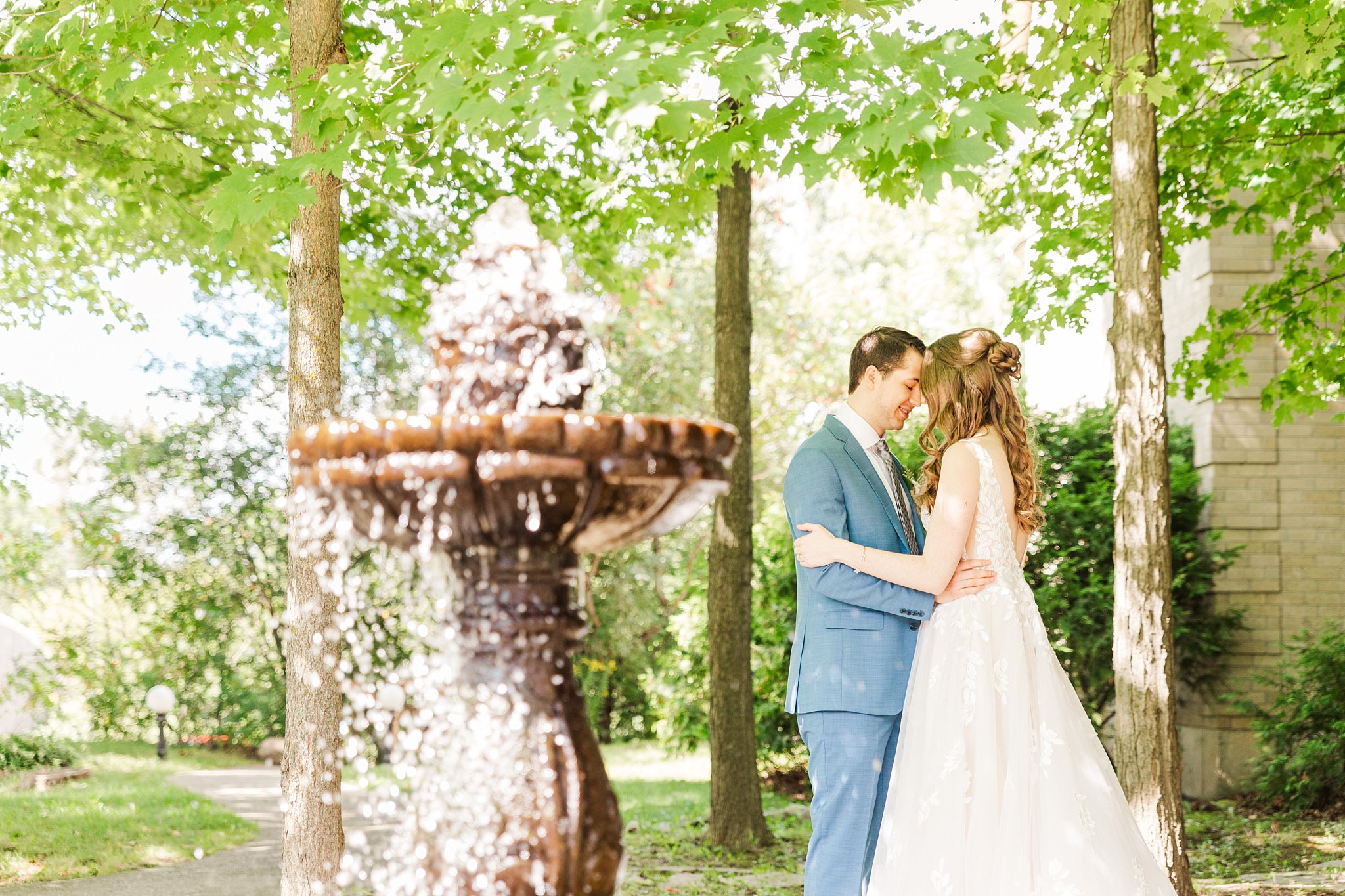a bride and groom stand together behind a fountain