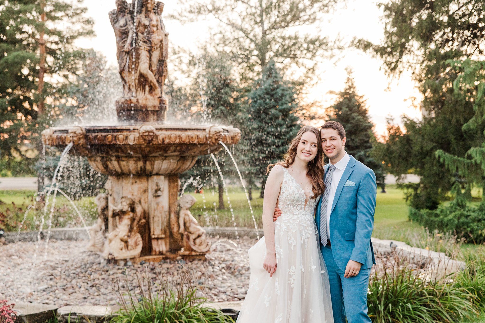 a bride and groom stand together in front of the fountain at the elm hurst inn