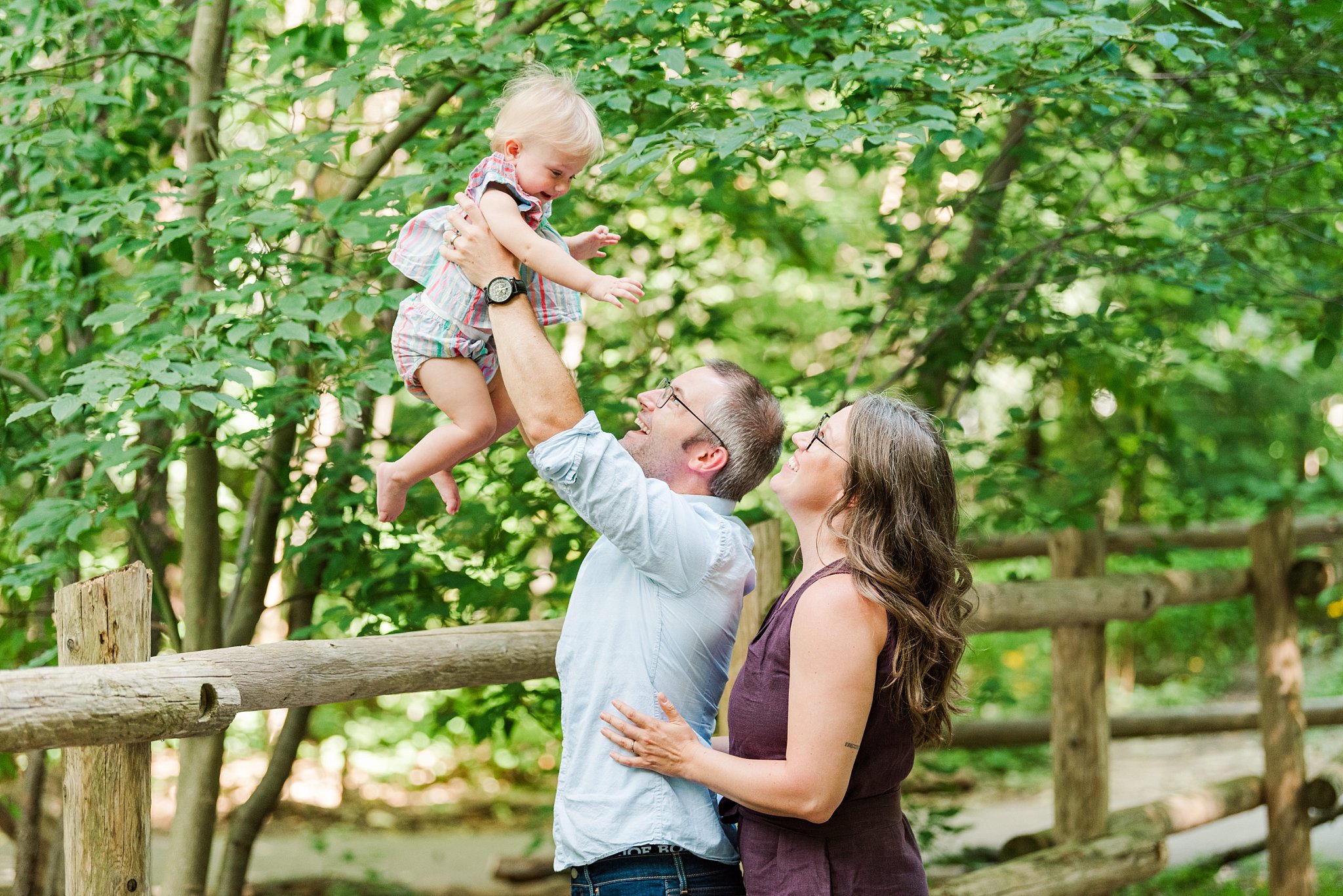 a dad lifts his daughter in the air while a mom smiles at them during their family photos london ontario
