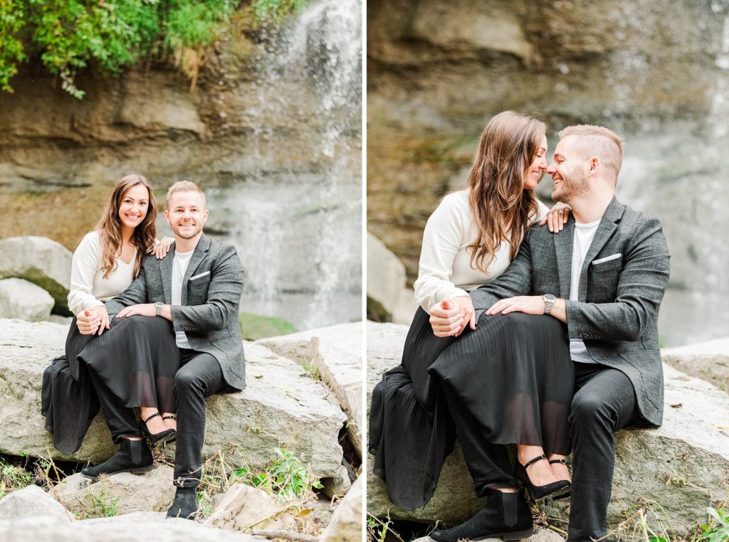 A couple sits on rocks together in front of a waterfall during their Kelowna Wedding Photographer engagement session