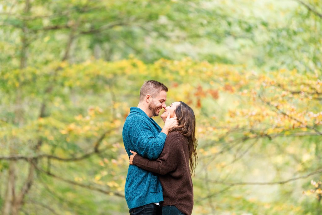 A couple kisses in front of a background of green and yellow trees by Kelowna Wedding Photographer Life is Beautiful Photography