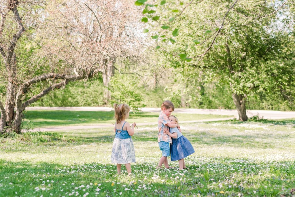 a little boy and two little girls play together in a patch of white flowers