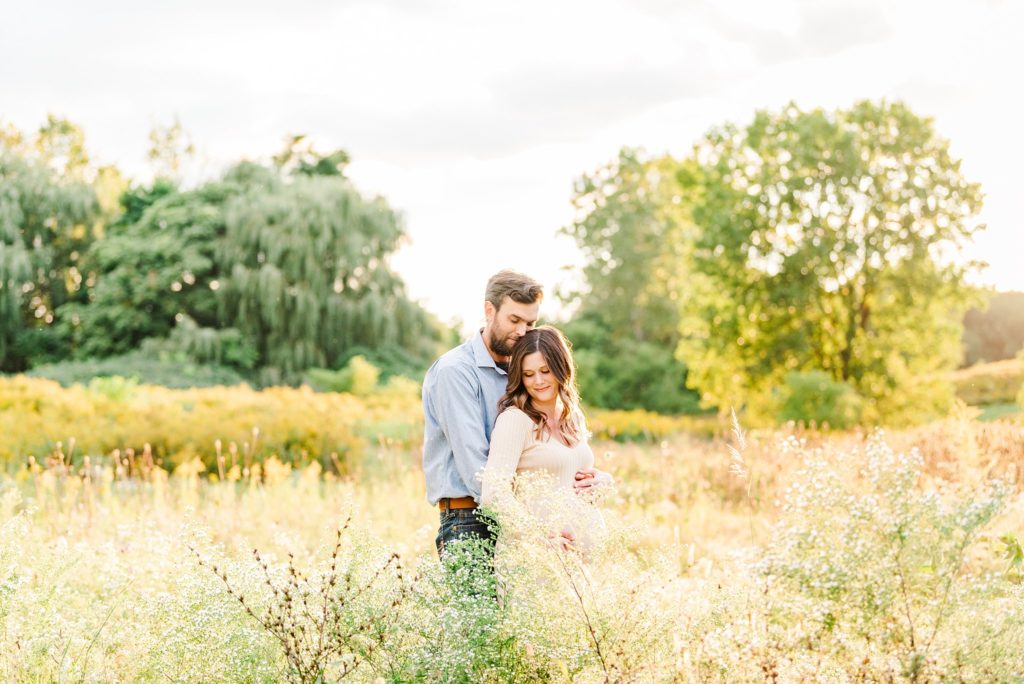 a couple stands together surrounded by tall grass and glowing yellow trees in the background at euston park