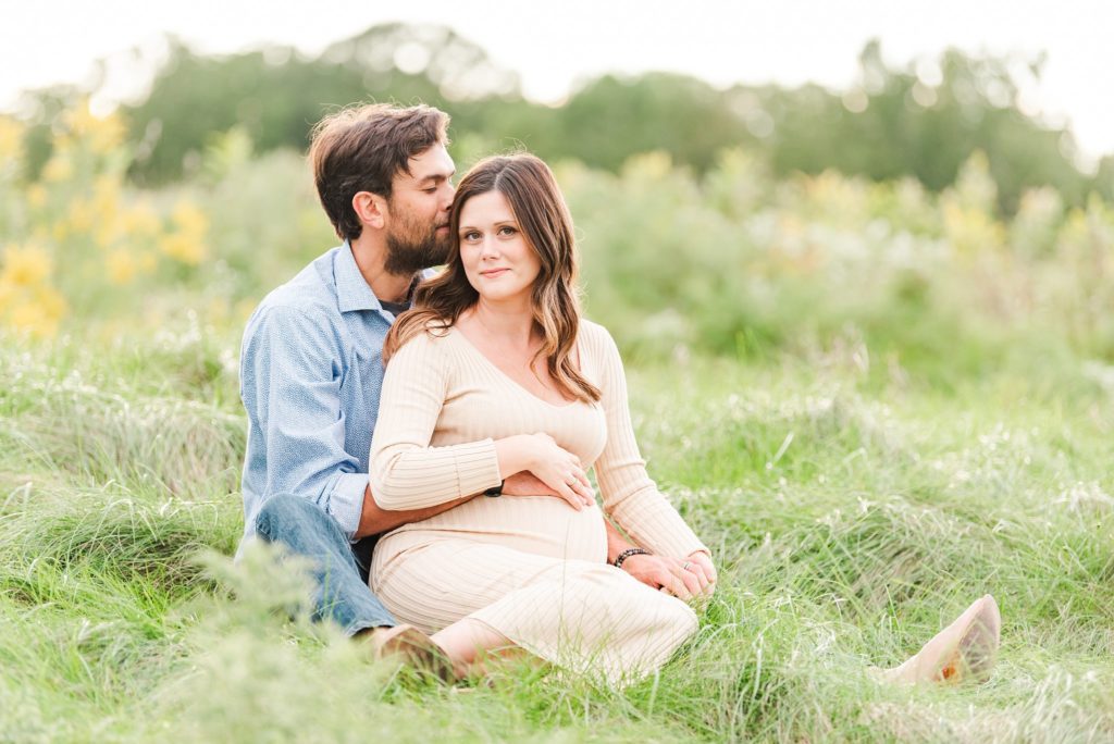 a man kisses his wife's forehead while she rests her hands on her baby bump during their maternity photos