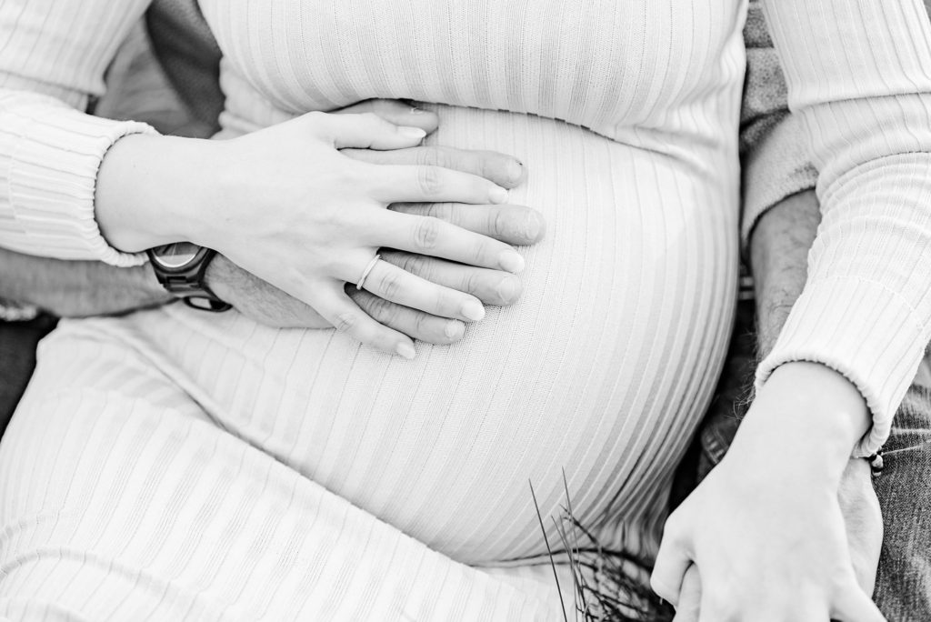 a black and white photo of a baby bump with hands resting on top