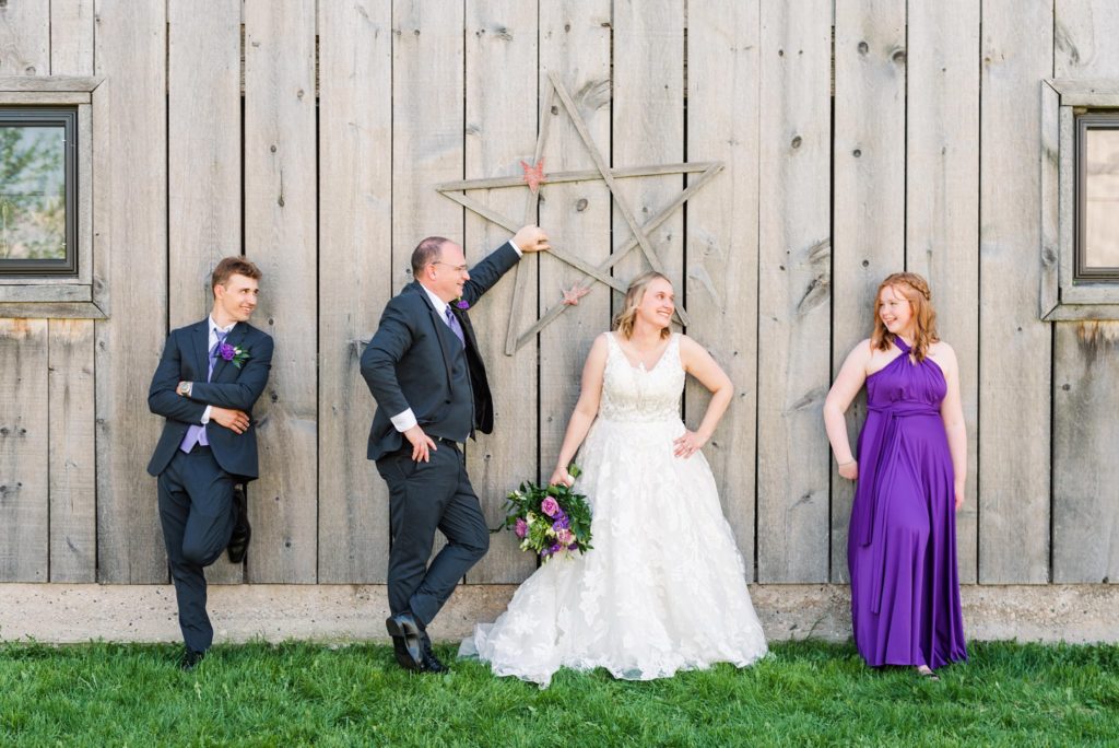 a wedding party stands against a wooden wall and laughs at each other