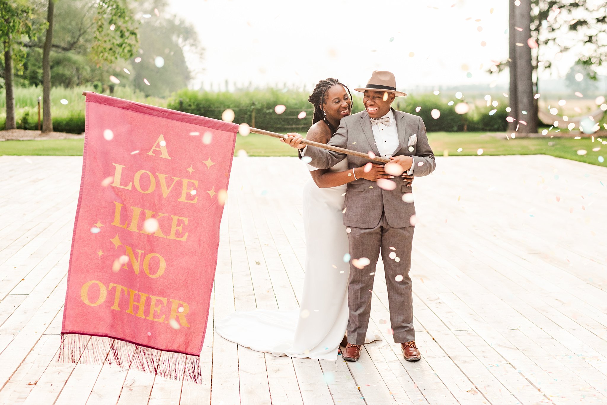 an lgbtqia+ couple laughs together while confetti swirls around them at wheatfield estate