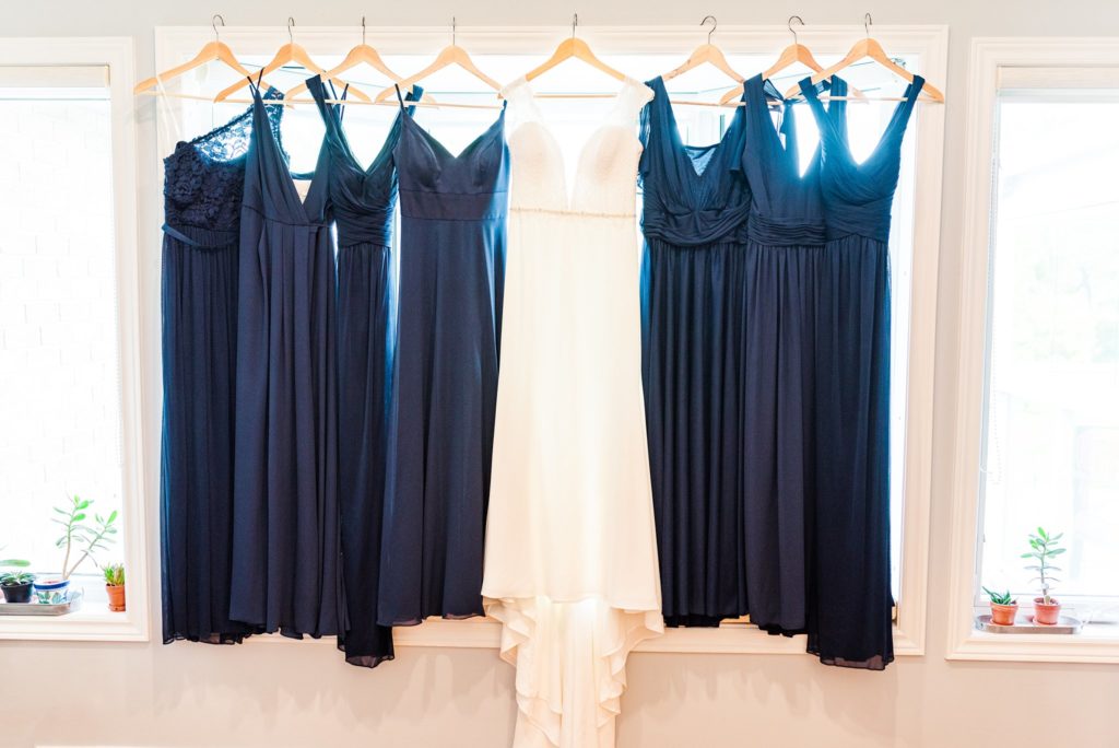 a wedding gown and navy blue bridesmaid dresses hang in a window