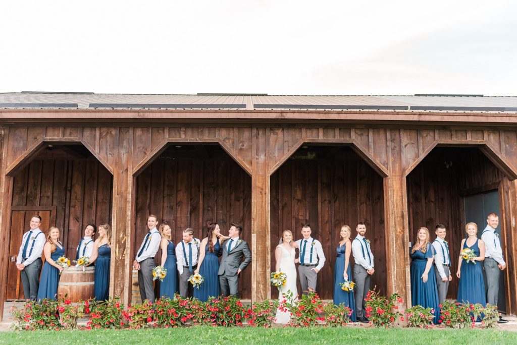 a wedding party stands in between wooden columns at a winery