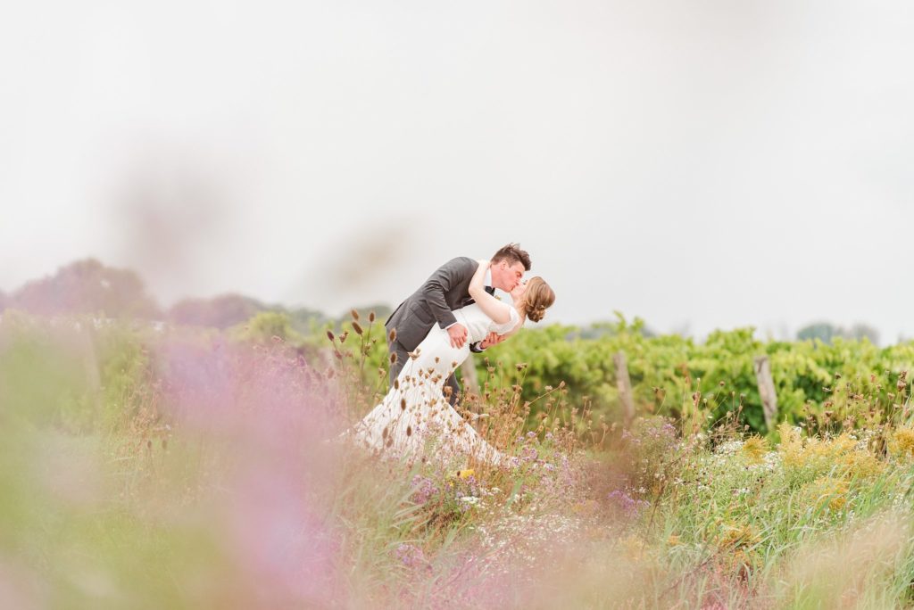 a bride and groom kiss while dipping backward, surrounded by wildflowers