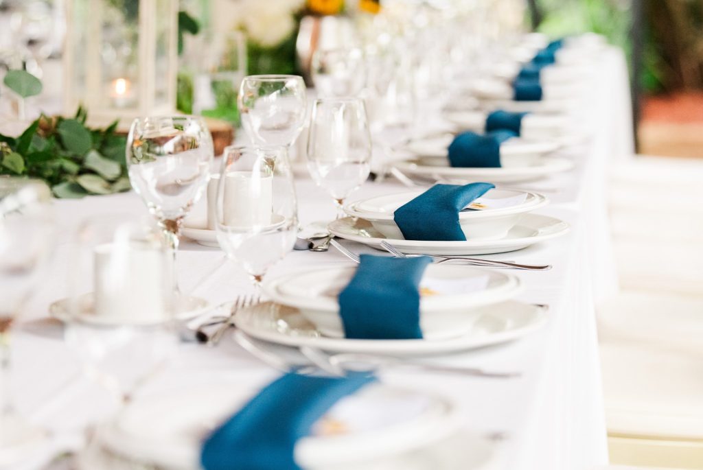 a row of plates with navy blue napkins for a club roma wedding reception
