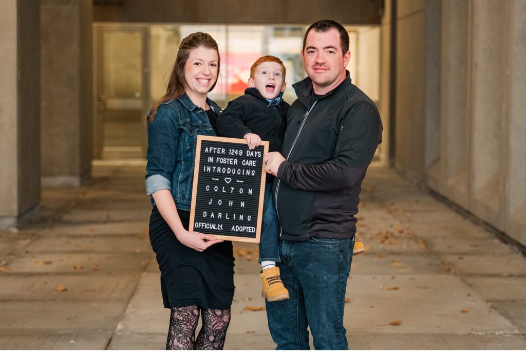 a family of 3 hold a letterboard sign celebrating an adoption